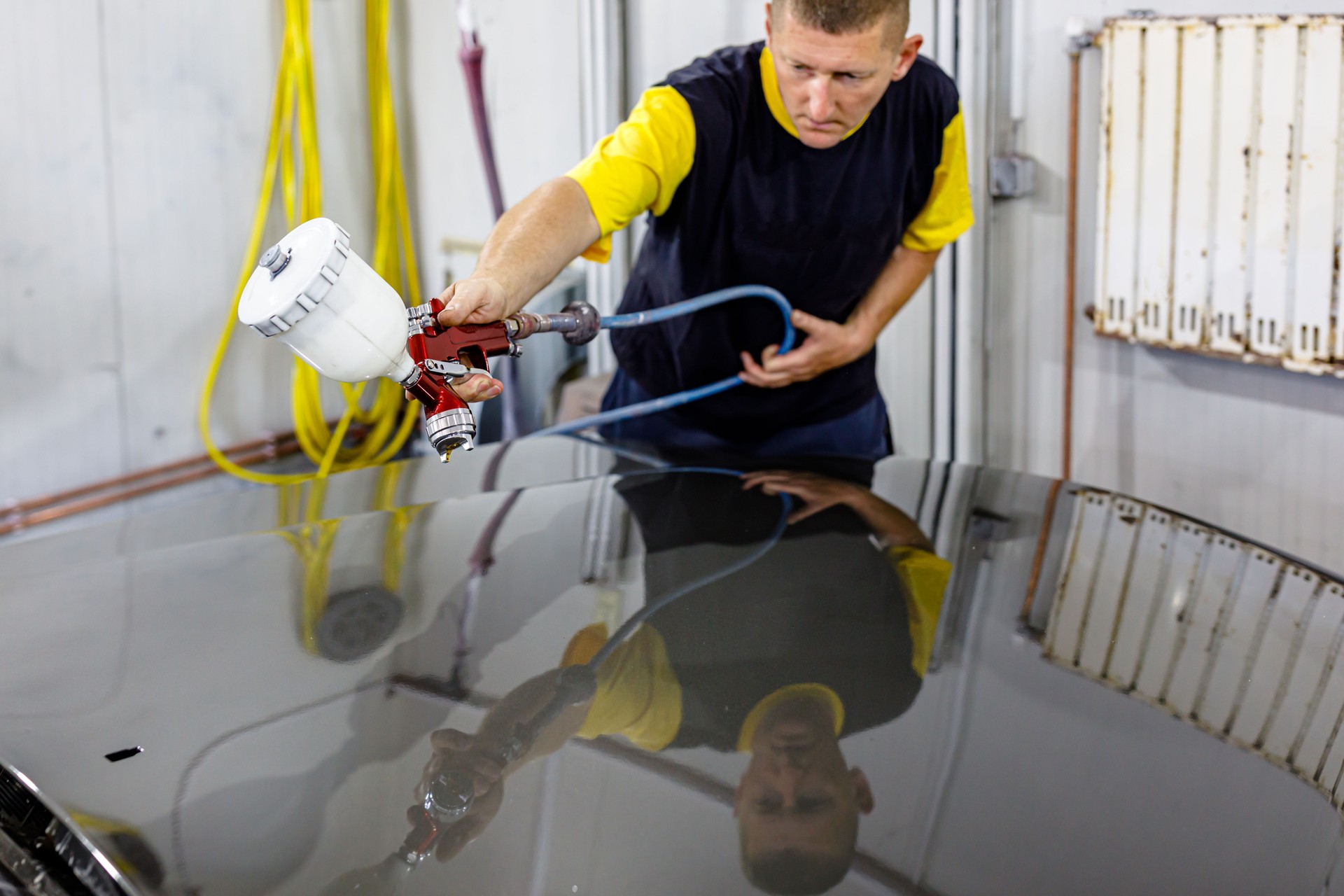 A Car Painter is Spraying the Car with Spraying Gas Compressor in a Car Service.